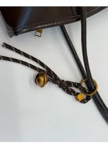 Detalle del bolso de cuero marrón oscuro con correa trenzada y adorno de campana