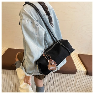 Detail of a large black canvas tote bag with brown leather lock charm on the shoulder