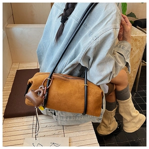 Detail of brown suede cylindrical shoulder bag with thin black leather straps and charm