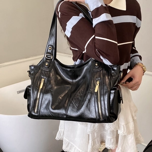 Detail of black glossy tote bag featuring parallel golden zippers and side pockets