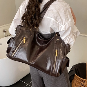 Detail view of coffee brown oil wax leather tote bag featuring gold zippers and side pockets