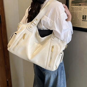 Detail view of creamy white tote bag featuring glossy texture and gold metallic zippers