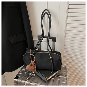 Detail view of black suede shoulder bag with mini brown charm on a metal suitcase