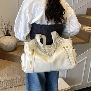Rear view of cream white tote bag with gold zippers worn by model in a cozy indoor setting