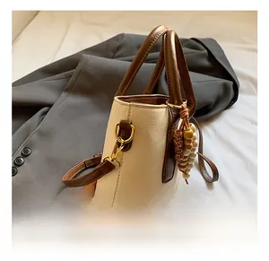 Détail de la quincaillerie dorée et du charme perlé sur le sac à main crème