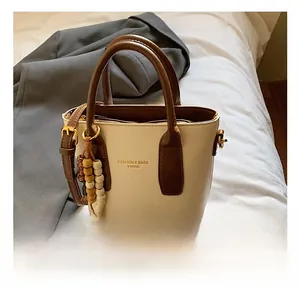 Détail du sac à main bicolore beige et marron avec breloque en perles de bois et logo doré