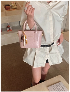 Détail d'un sac à main en cuir rose avec pompon en perles de bois et lettrage doré chic