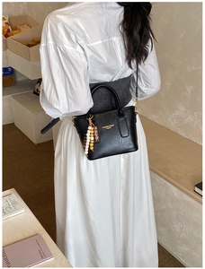 Détail du sac seau en cuir noir avec imprimé mode et ornement de pompon en perles de bois