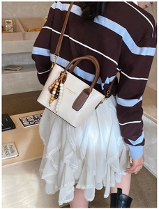 Détail d'un sac seau beige et marron avec pompon en perles et logo de mode élégant