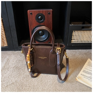 Détail du sac seau en cuir marron foncé avec lettrage doré et breloque en perles