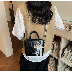 Detalle de bolso cubo negro brillante con corazón de perlas y lazo sobre chaleco beige