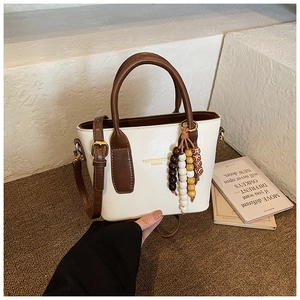 Détail du sac cabas crème avec anses brunes, pendentif en bois et bandoulière