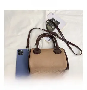 Mini Boston bag with brown leather trim and shoulder strap shown beside a smartphone