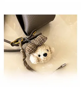 Close-up of fluffy apricot poodle charm with checkered bow on brown leather handbag