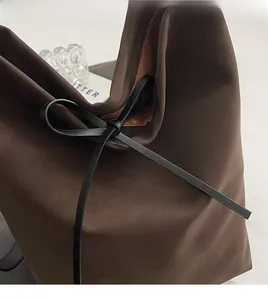 Détail du cabas marron foncé avec un nœud décoratif noir et une texture de cuir mate