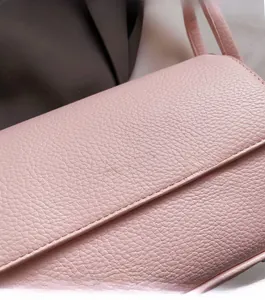 Close-up of light pink lychee grain leather texture and metallic logo on the handbag