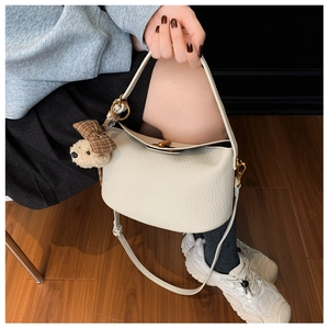 Detail of off-white lychee leather handbag with cute teddy bear charm and strap