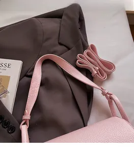 Detail of pink lychee grain leather shoulder bag with adjustable strap on white fabric