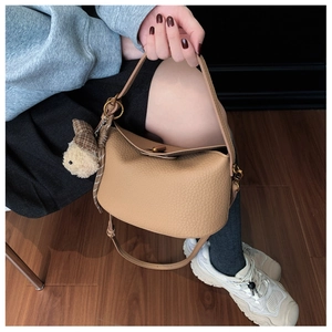 Detail of khaki pebbled leather bucket bag with plush rabbit charm and shoulder strap
