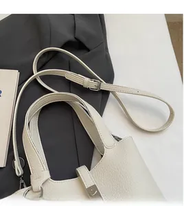 Detalle de bolso tipo cubo en cuero granulado crema con correas ajustables y herrajes plata