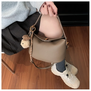 Close-up of brown pebbled leather bucket bag with gold hardware and cute teddy bear charm
