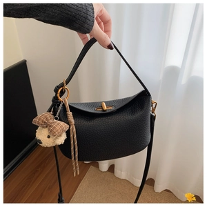 Close-up of black lychee grain leather bag with gold twist lock and teddy bear charm