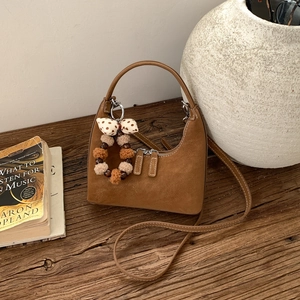 Detail of a brown suede moon bag on vintage wood with a plush charm and strap