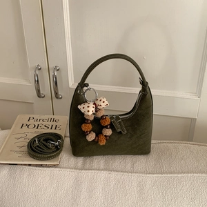 Detailed close-up of dark green dumpling bag with plush charm and long shoulder strap