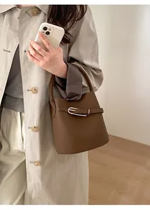 Détail du sac seau marron en cuir avec boucle métallique argentée porté par un mannequin