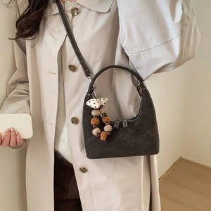 Deep brown suede crescent bag with plush charm and strap detail on a beige trench coat