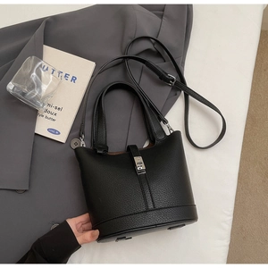 Detalle de bolso cubo de cuero negro con hebilla plateada y correa bandolera