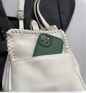 Détail des bords tressés et de la poche avant du sac seau crème avec un smartphone