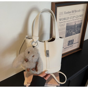 Detalle de bolso cubo blanco roto con textura de cuero, cierre plateado y colgante conejo