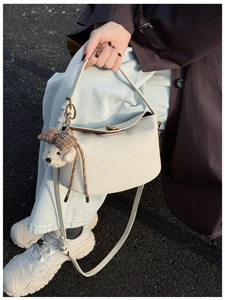 Detail of cream white litchi grain leather handbag with cute teddy bear charm and gold clasp