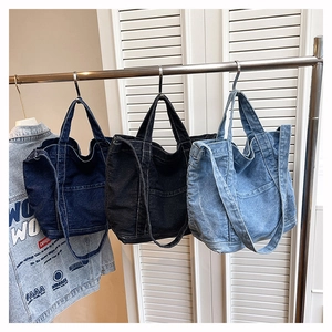 Detailed view of three denim tote bags in dark blue, black, and light blue on hangers
