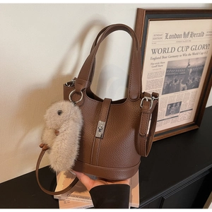 Primer plano del bolso cubo de cuero marrón con cierre plateado y colgante de conejo de peluche