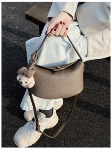 Detail of khaki lychee leather handbag with metal turn-lock and plush bear charm