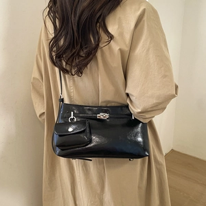 Dettaglio della borsa a spalla nera lucida con chiusura a scatto su trench beige