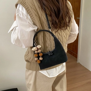 Detail of black suede crescent bag with white contrast stitching and fuzzy ball keychain
