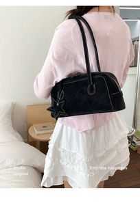 Detail of black Boston baguette bag featuring white contrast stitching and a star charm