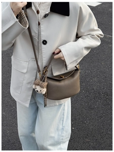Detail of dark brown lychee textured leather crossbody bag with a plaid bear charm