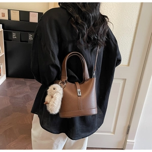 Bolso tipo cubo marrón con grano de lichi y un tierno colgante de peluche en un interior
