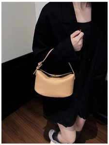 Detail of light beige lychee pattern leather handbag showing unique crescent shape and strap