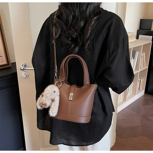 Bolso cubo de cuero marrón con cierre plateado y colgante de conejo de peluche en modelo