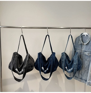 Three colors of denim tote bags with REPLACED text hanging on a display rack