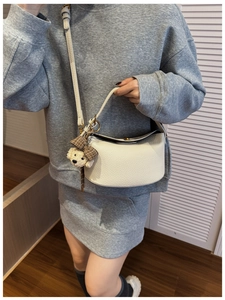 Detail of off-white lychee pattern leather handbag with plush puppy charm on strap
