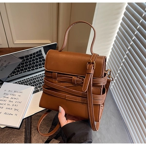 Vue détaillée d'un sac bandoulière en cuir marron avec sangles décoratives sur un bureau