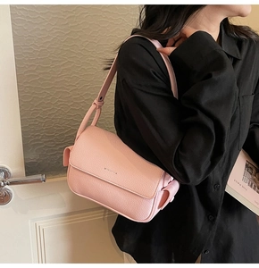 Close-up of pink pebbled leather crossbody bag featuring a soft bow detail and magnetic flap