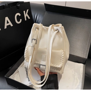 Détail du sac seau blanc avec rabat tissé et boucle argentée dans un coffret cadeau chic