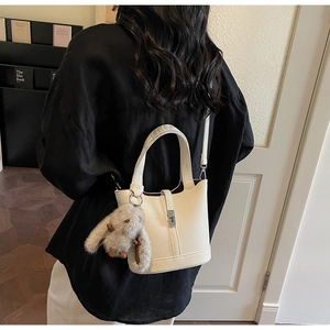Detalle del bolso de cubo crema con hebilla metálica y colgante de conejo de peluche
